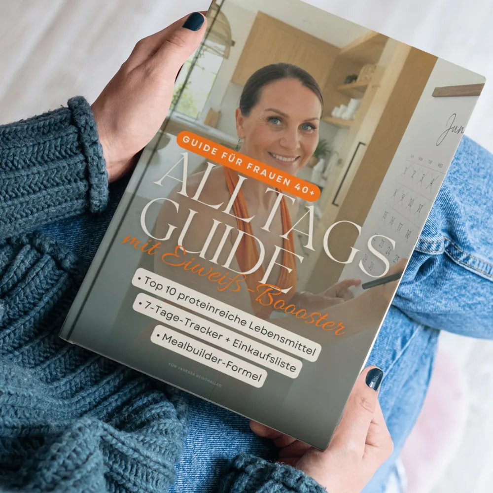 Buch mit Titel „Alltagsguide mit Eiweiß-Booster“ und Untertitel „Guide für Frauen 40+“ mit Infos zu proteinreichen Lebensmitteln, 7-Tage-Tracker und Einkaufsliste, gehalten von Person in blauer Kleidung