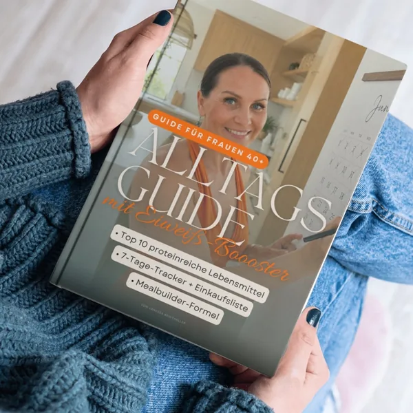 Buch mit Titel „Alltagsguide mit Eiweiß-Booster“ und Untertitel „Guide für Frauen 40+“, gehalten von einer Person in blauer Kleidung